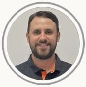 Headshot of a smiling man with short dark hair and beard in a gray shirt with an orange collar