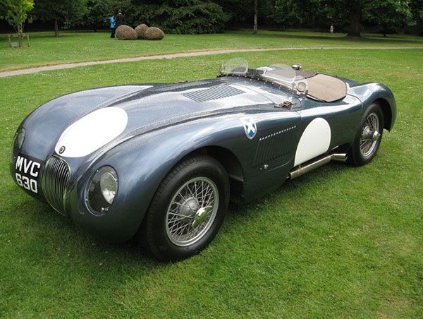 Vintage dark green open-top roadster with white accents parked on grass in a park