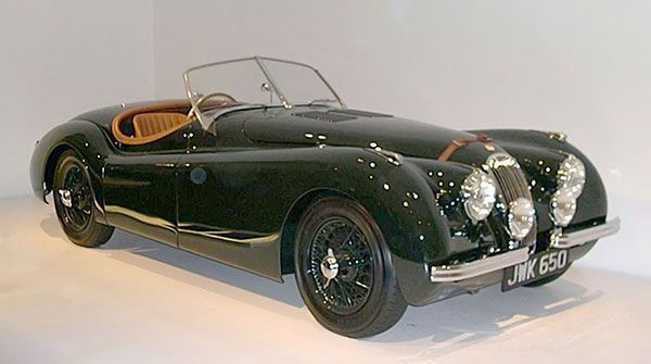Classic dark green vintage convertible sports car with tan interior, shown in a studio setting
