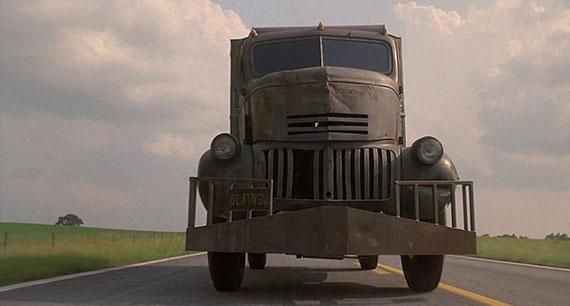 Front view of a dark vintage truck driving on a rural road under a cloudy sky
