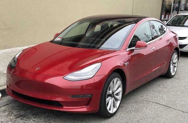 Red Tesla sedan parked outdoors beside a building.