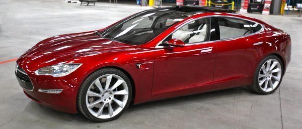 Red Tesla sedan parked indoors at an auto show, side view