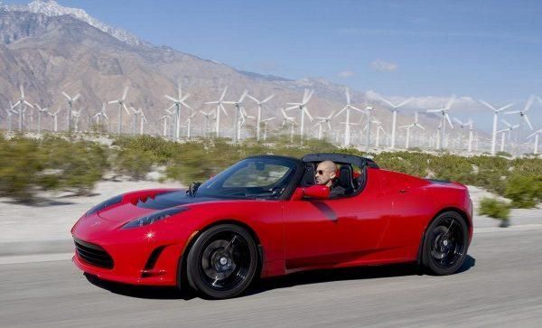 Red sports car driving on a road with wind turbines and mountains in the background
