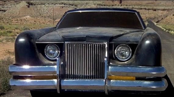 Front view of a black vintage luxury car parked on a road, with chrome grille and round headlights