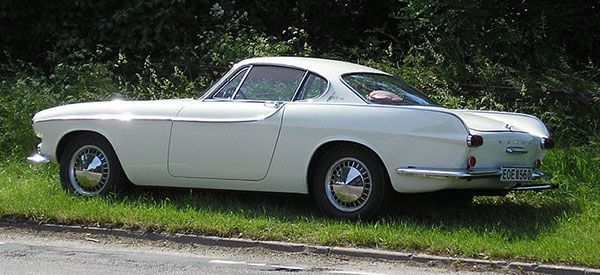 Classic white vintage coupe parked on a grassy roadside.
