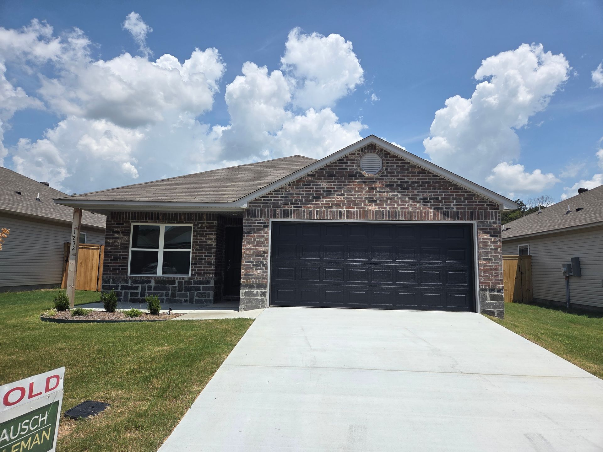 A brick house with a black garage door and a sold sign in front of it.