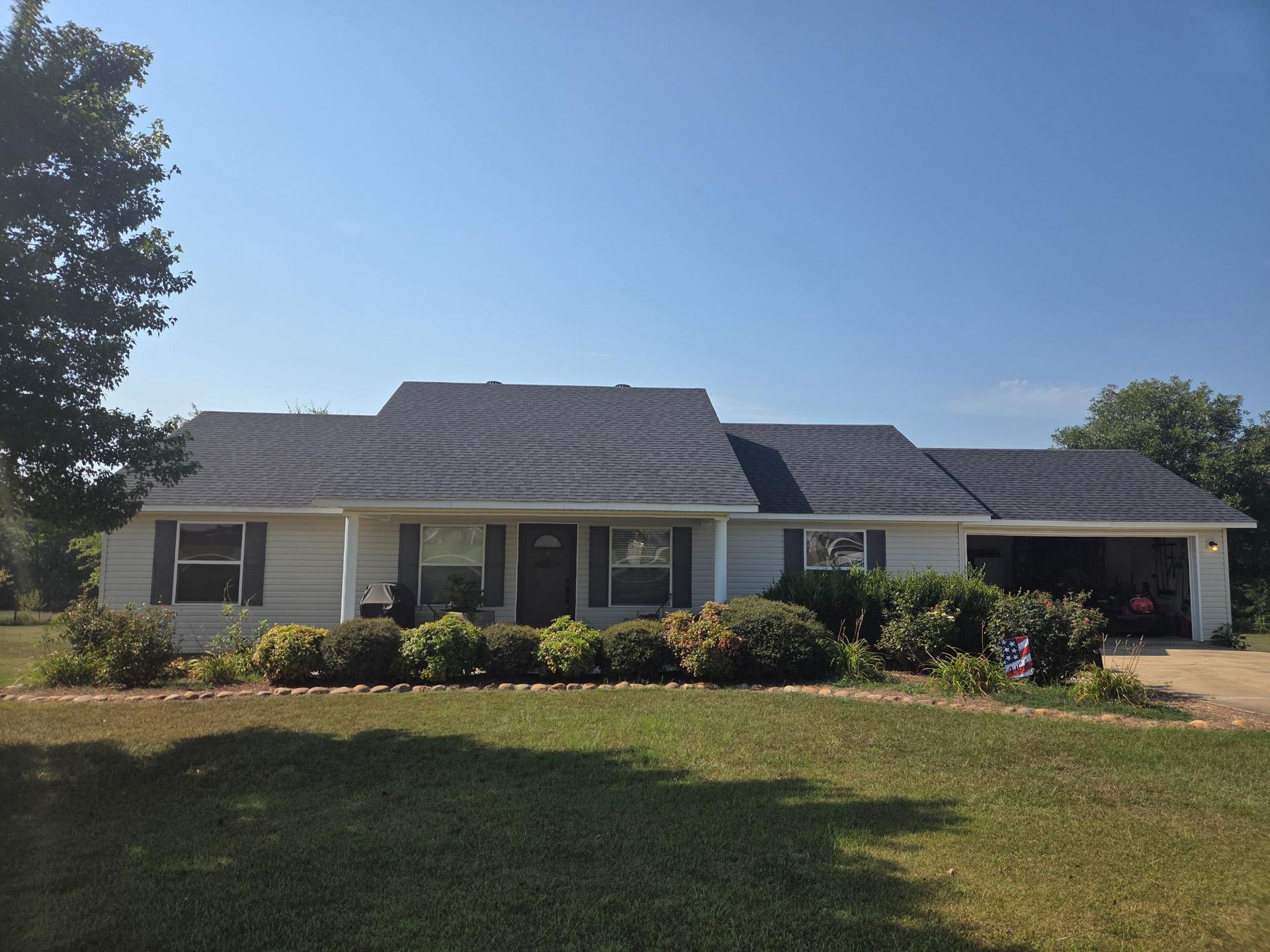 White house with dark roof and garage; bushes in front, blue sky.