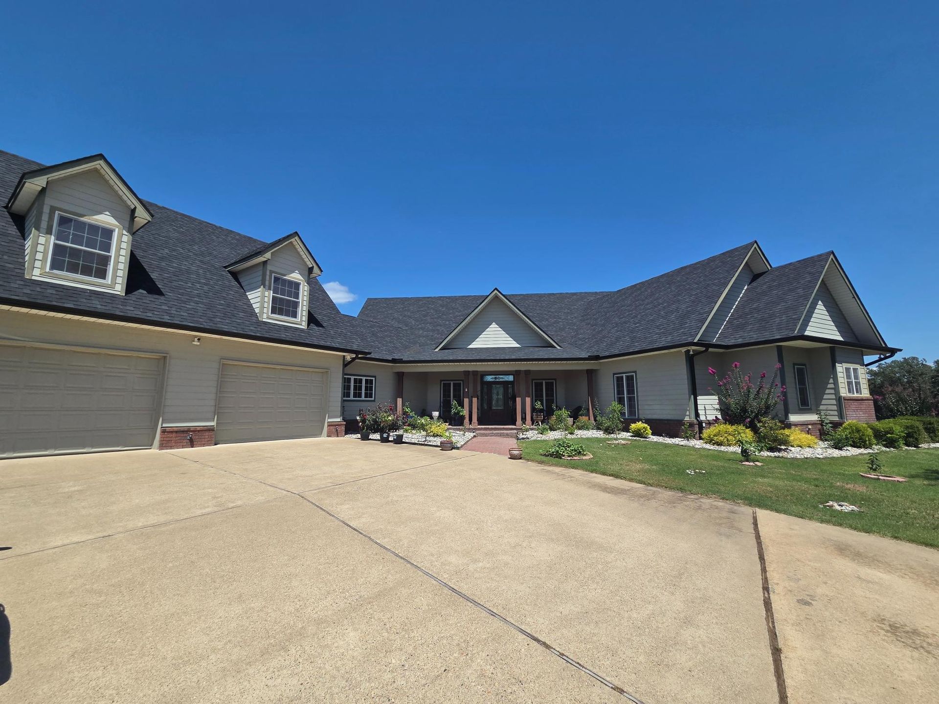 A light-colored house with a dark roof and a long driveway under a blue sky.