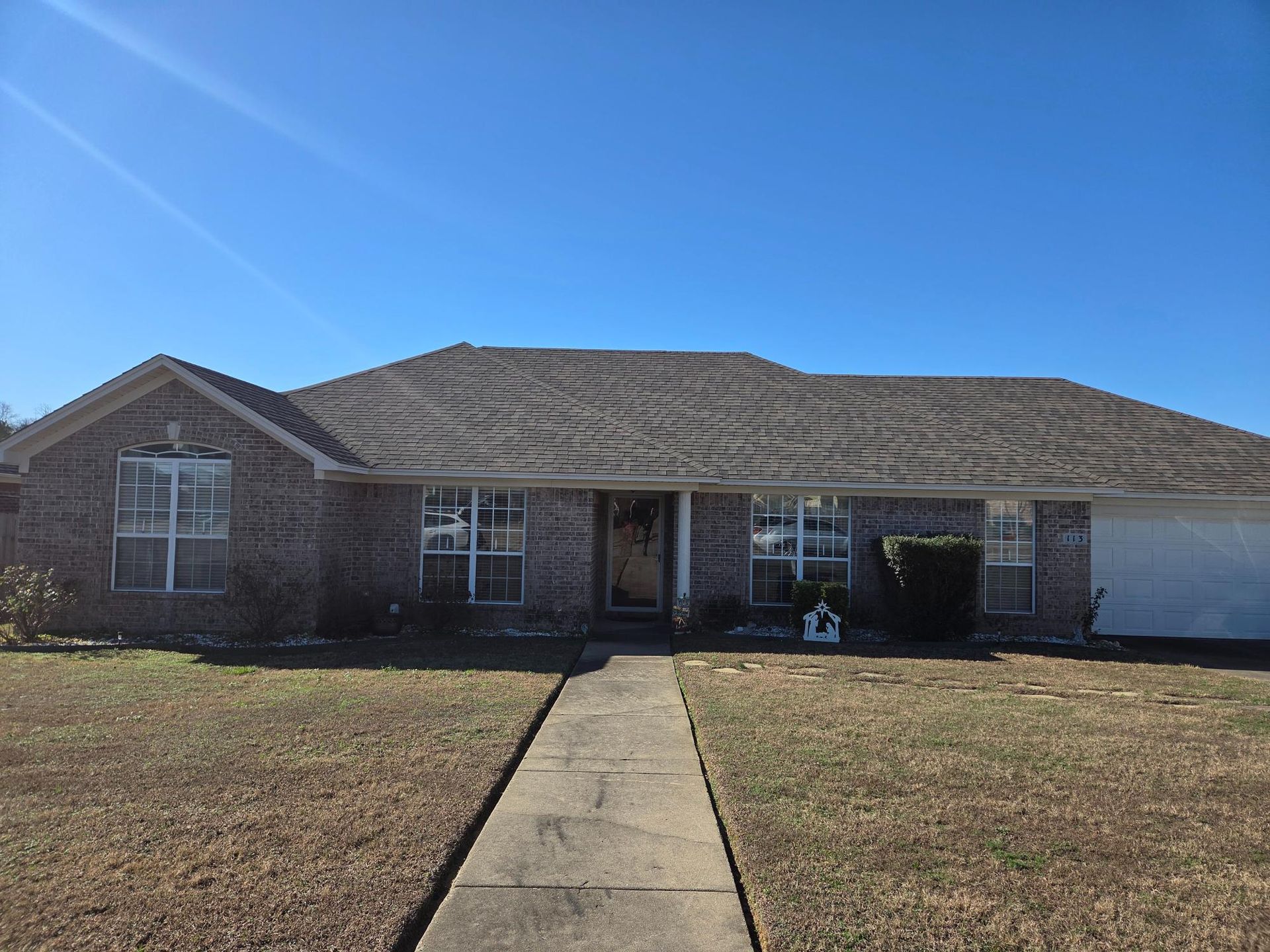Brick house with a gray roof and a concrete walkway, on a sunny day.