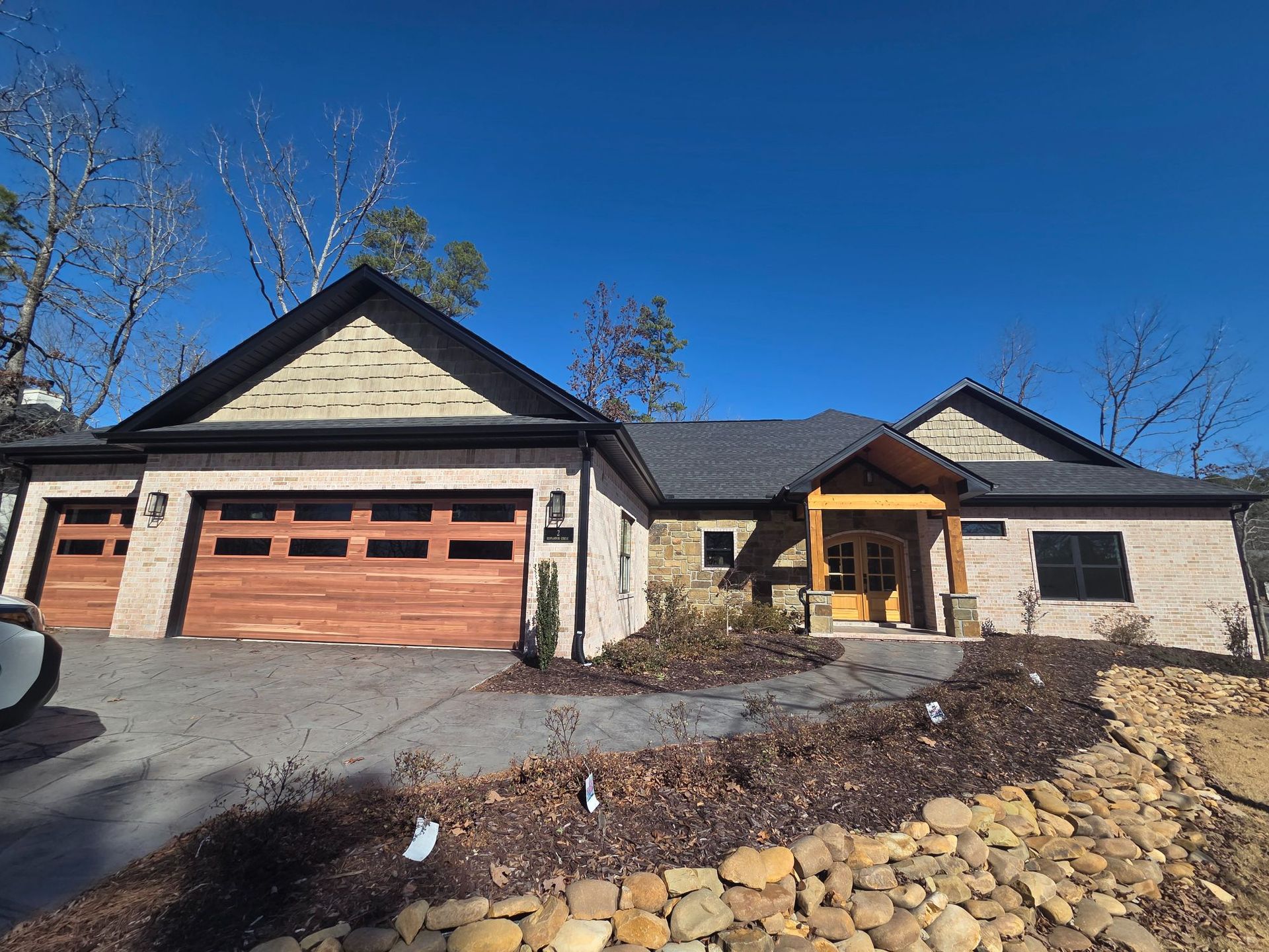 House exterior with tan brick, brown garage doors, and a wood-beamed entryway under a clear blue sky.
