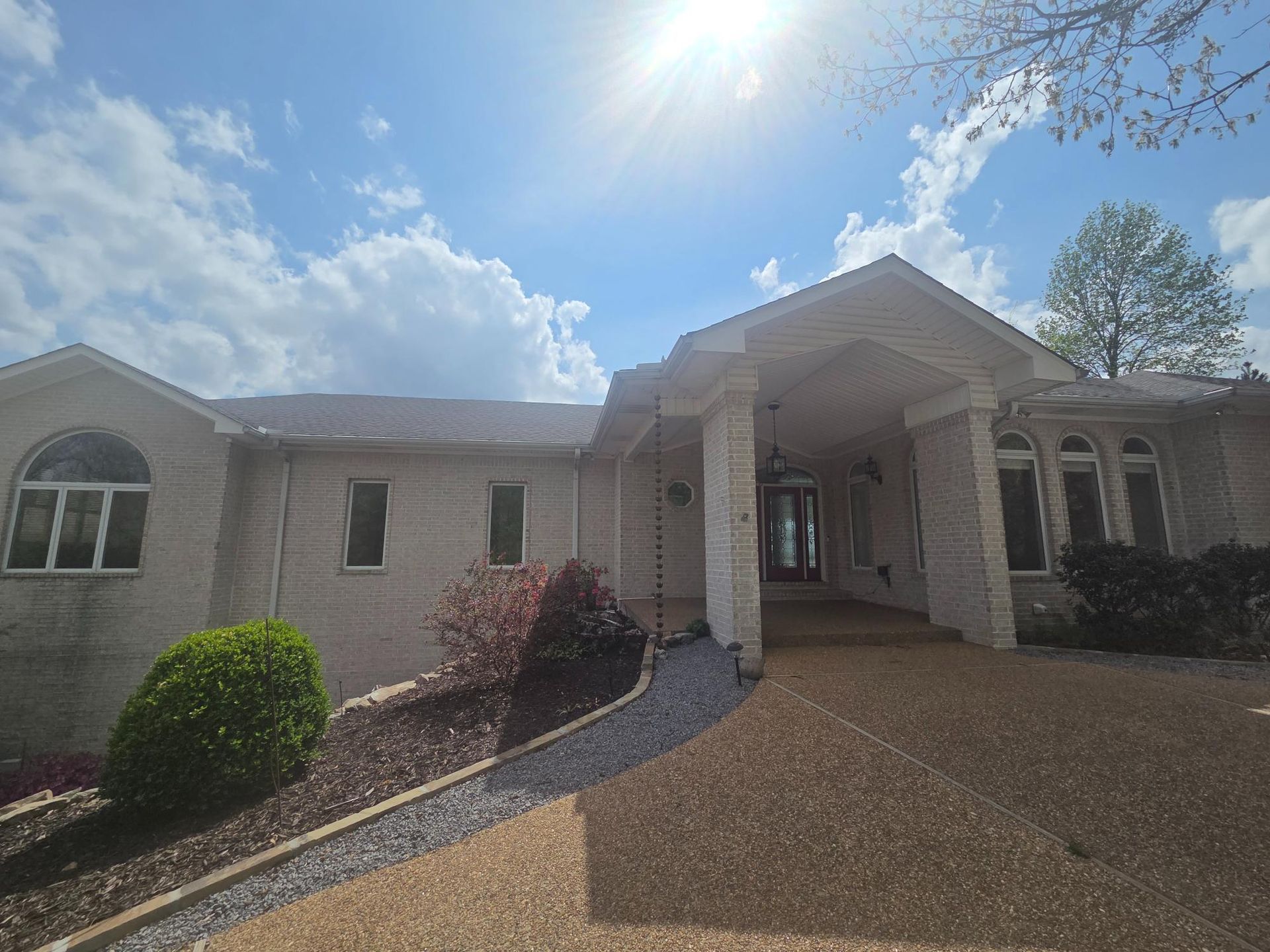 Light-colored brick house with a covered entryway and large arched windows under a bright, sunny sky.