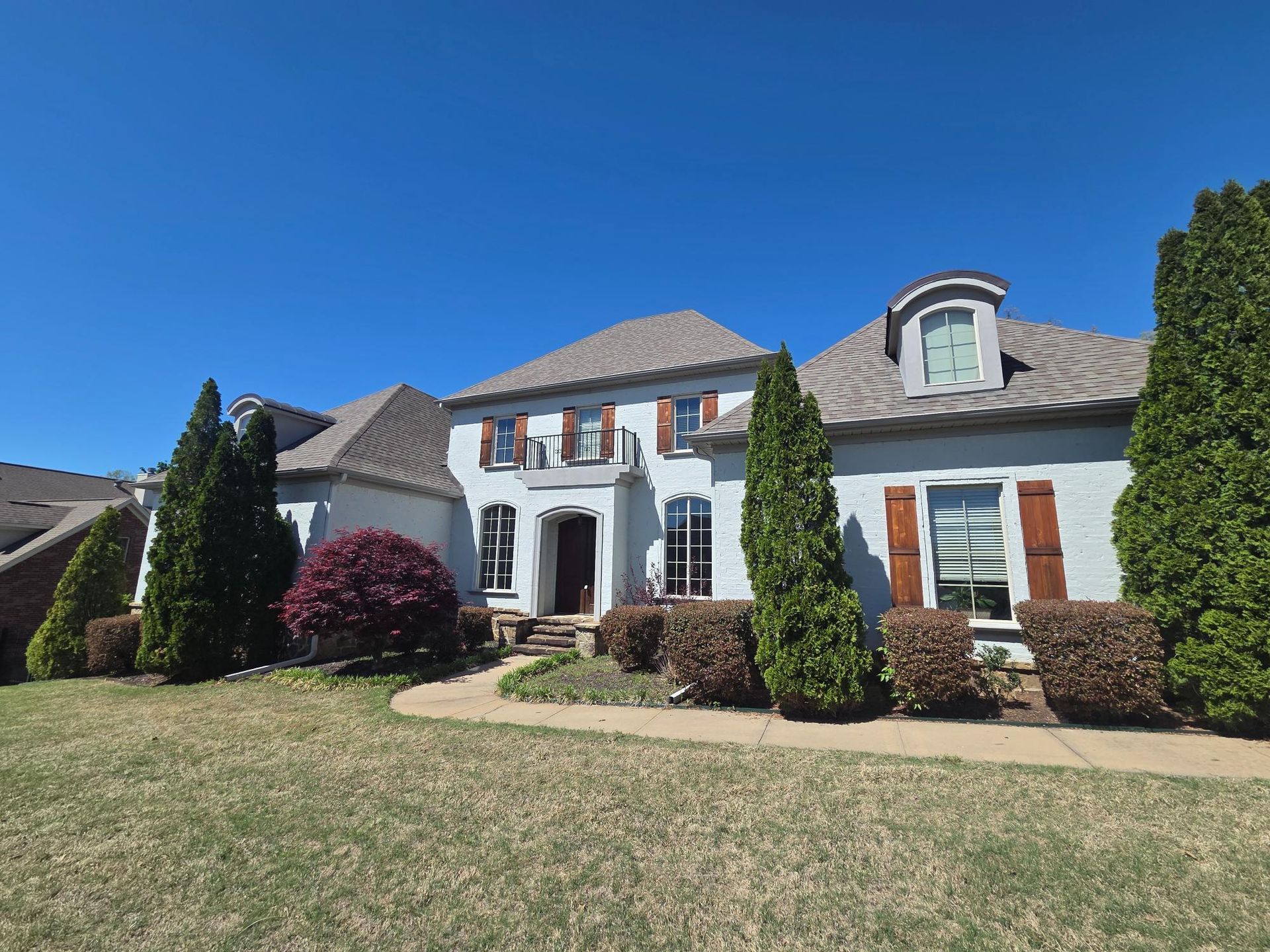 A large, light-gray two-story house with brown shutters and a gray roof, set against a clear blue sky.