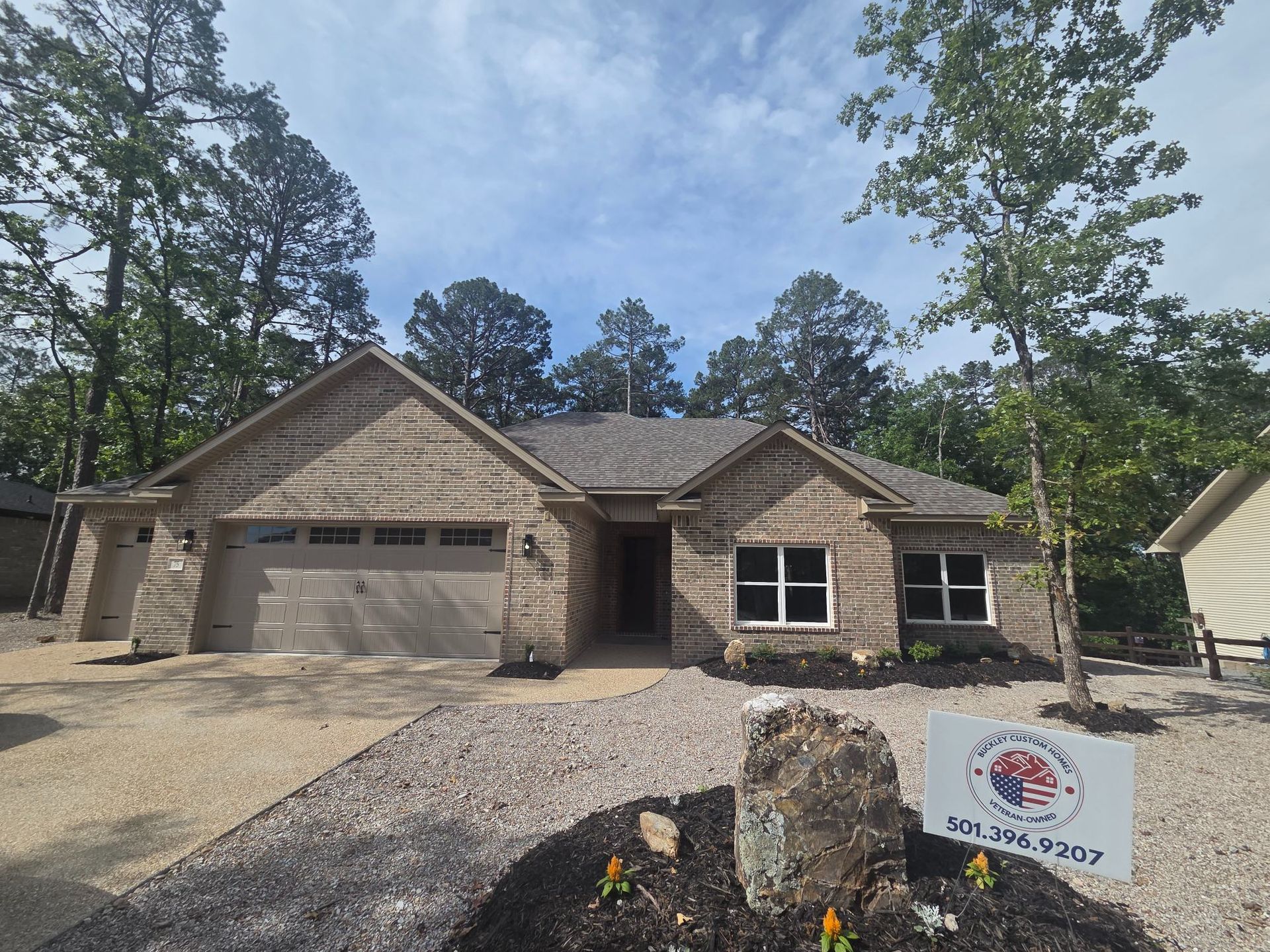 New brick house with two-car garage, stone accents, and a landscaping sign in front.