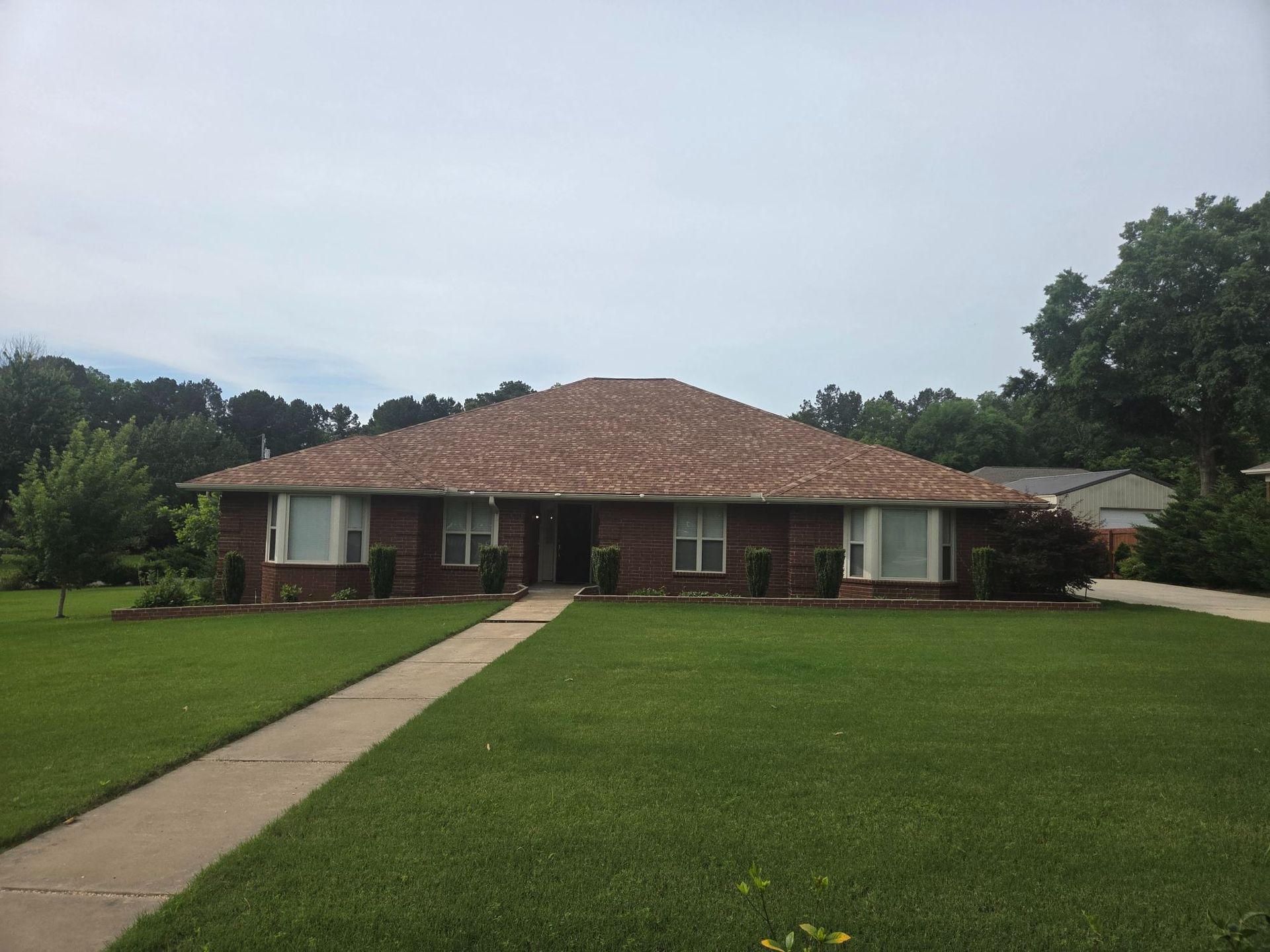 Single-story brick house with a large lawn and concrete walkway under a cloudy sky
