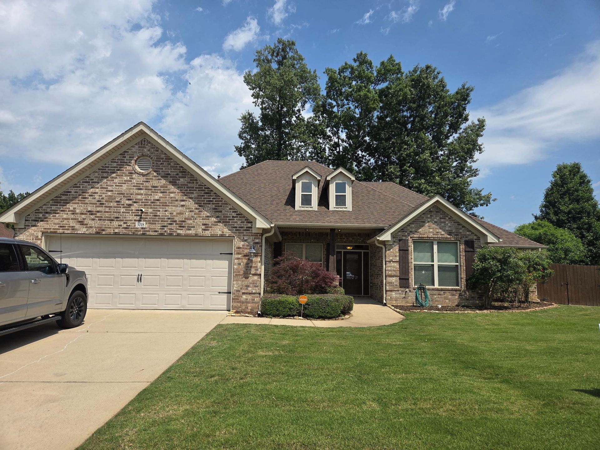 Suburban brick house with two-car garage, green lawn, and partly cloudy sky
