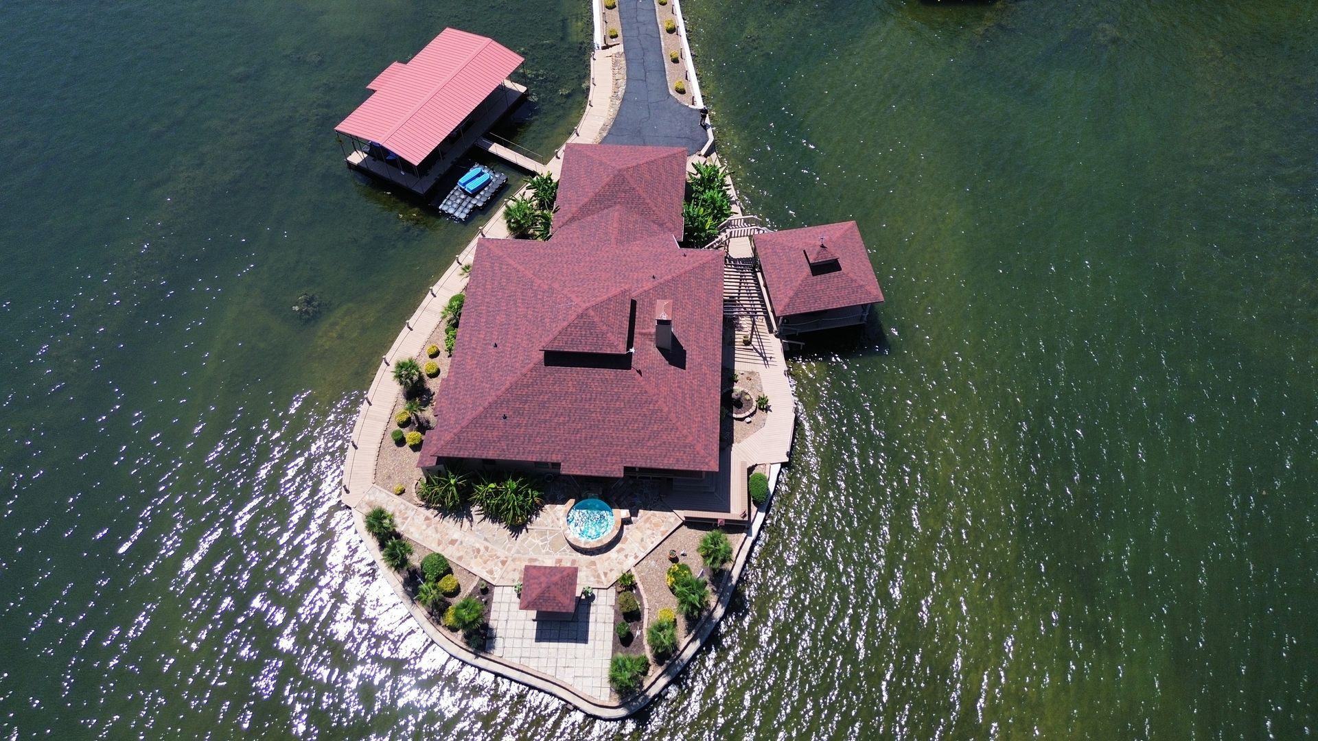 Aerial view of a lakeside house with a red roof and dock on clear green water