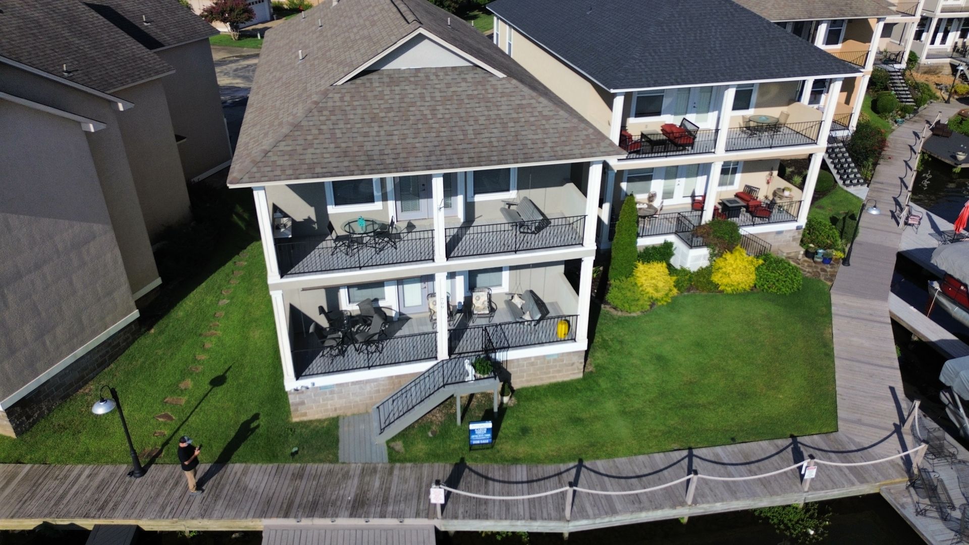 Aerial view of a modern beachfront house with balconies, lawn, and a boardwalk fence by the water.
