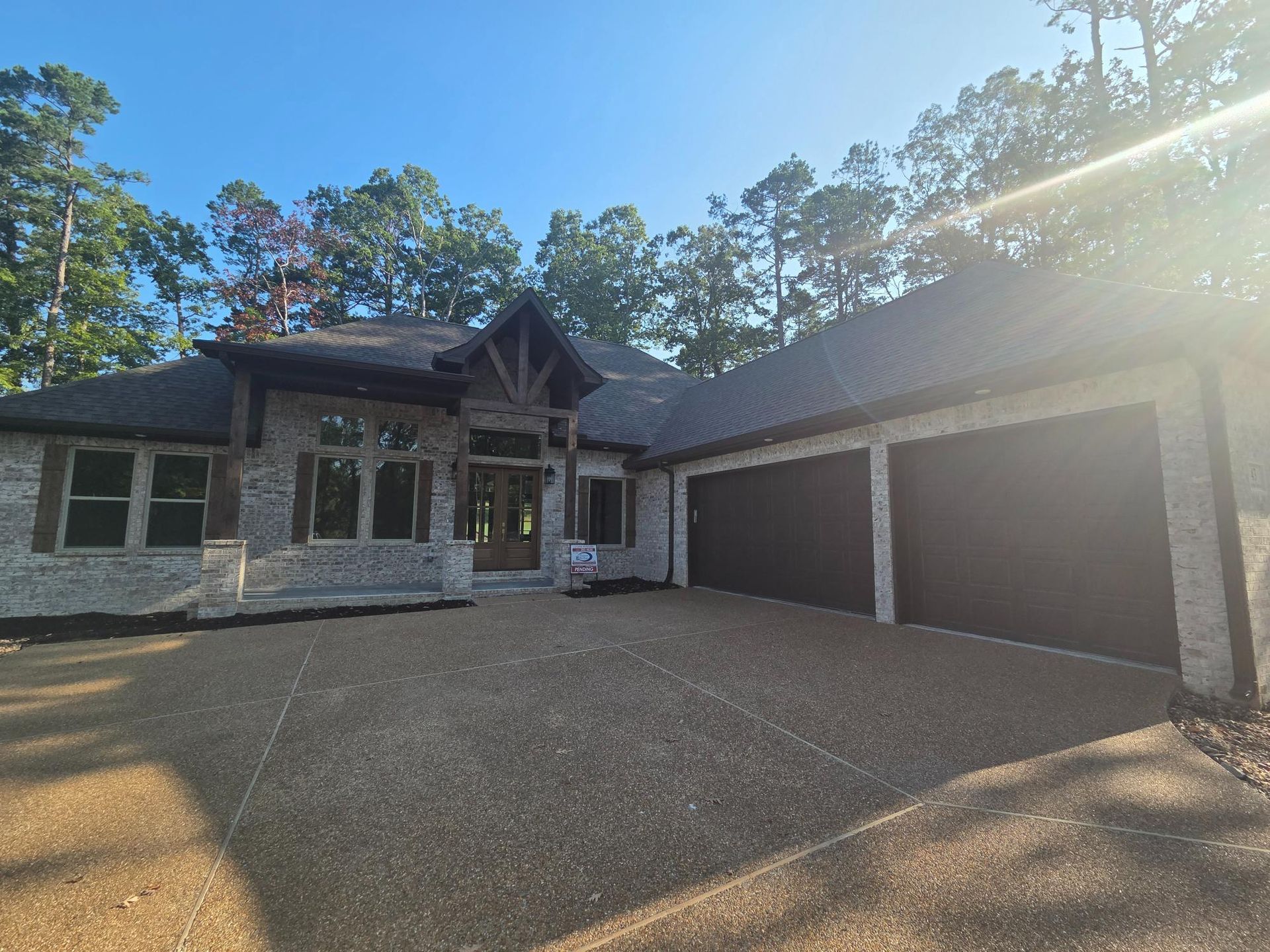 Exterior of a brick home with a gravel driveway and two-car garage under a bright sky.