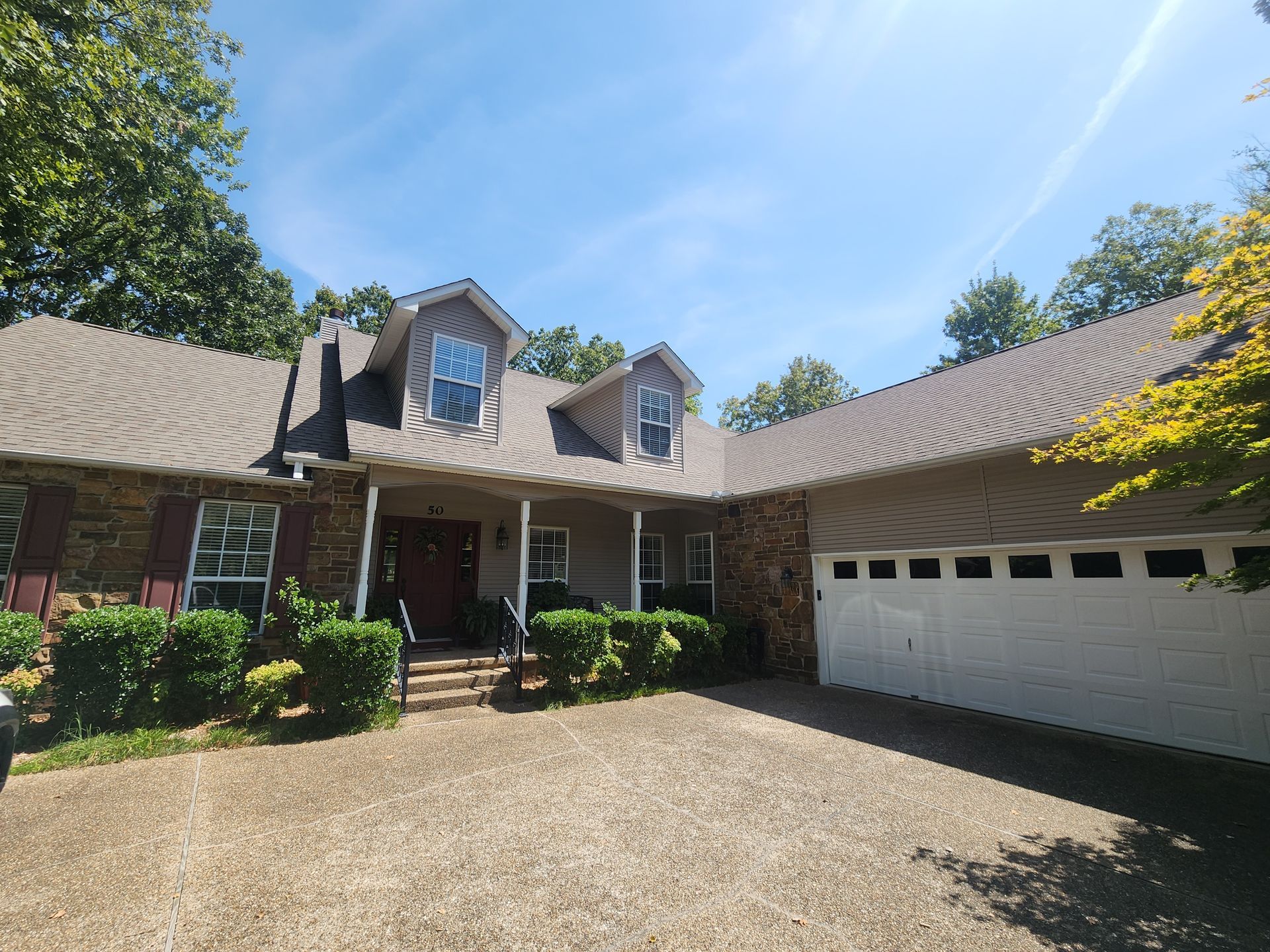 Brick house with dormer windows, front porch, and attached white garage under a clear blue sky