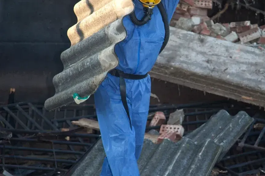 A man in a blue jumpsuit is carrying a large piece of asbestos.