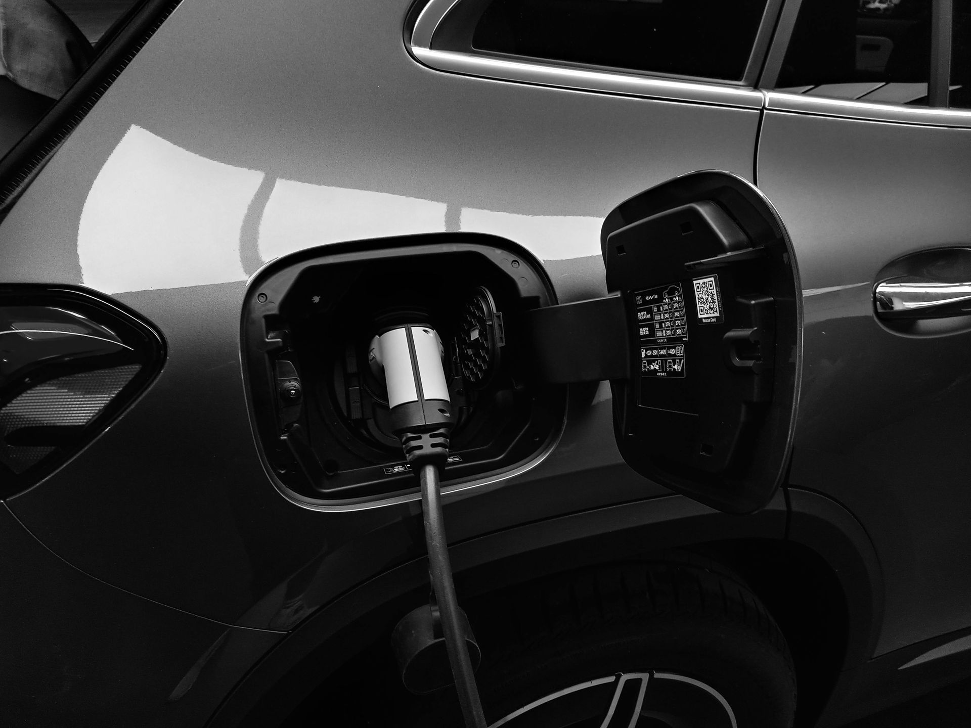 A black and white photo of an electric car being charged.