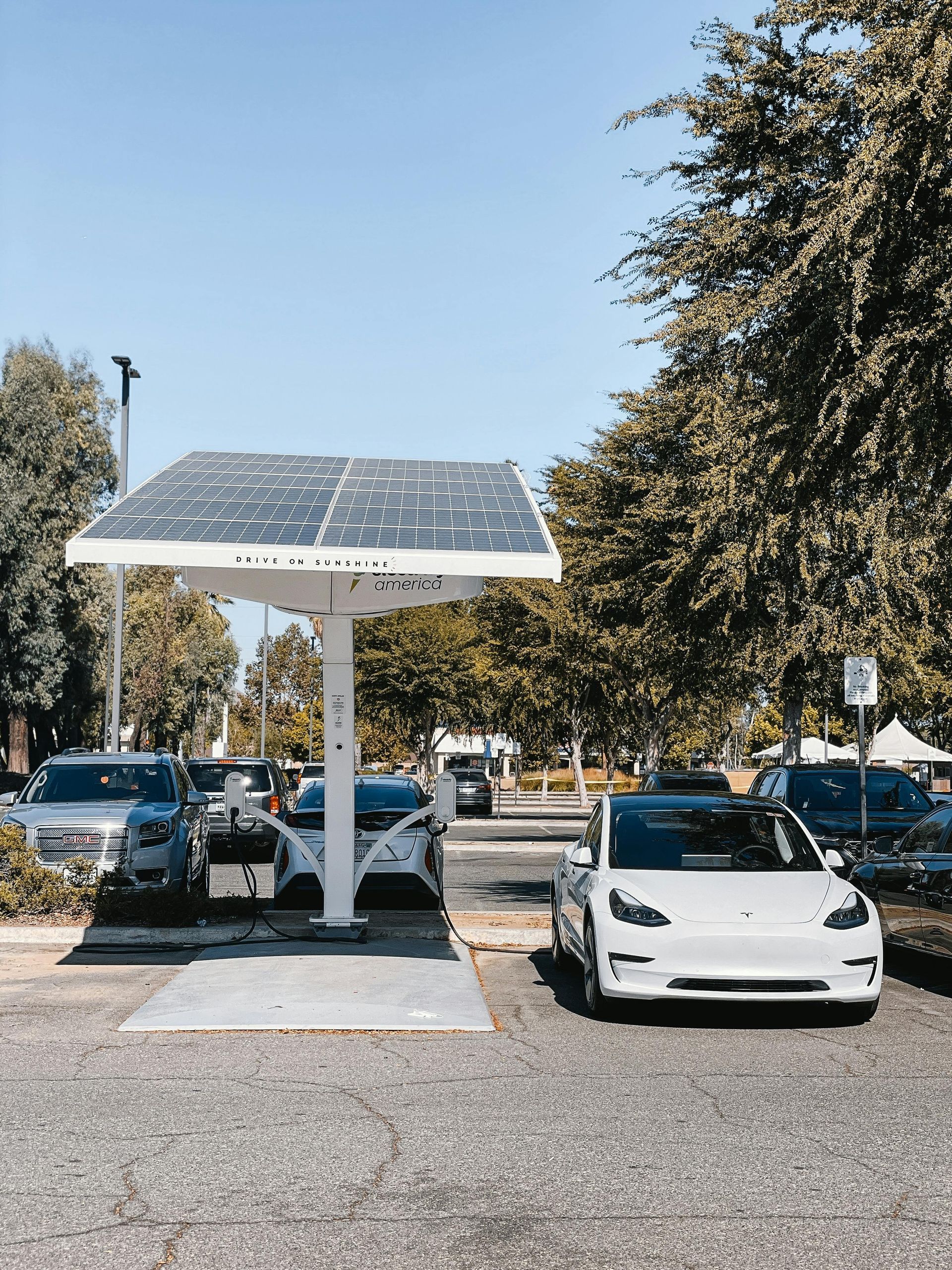 A row of cars are parked under a solar panel in a parking lot.