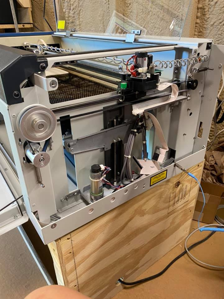 Internal view of an industrial laser cutter machine sitting atop a wooden base in a workshop setting.