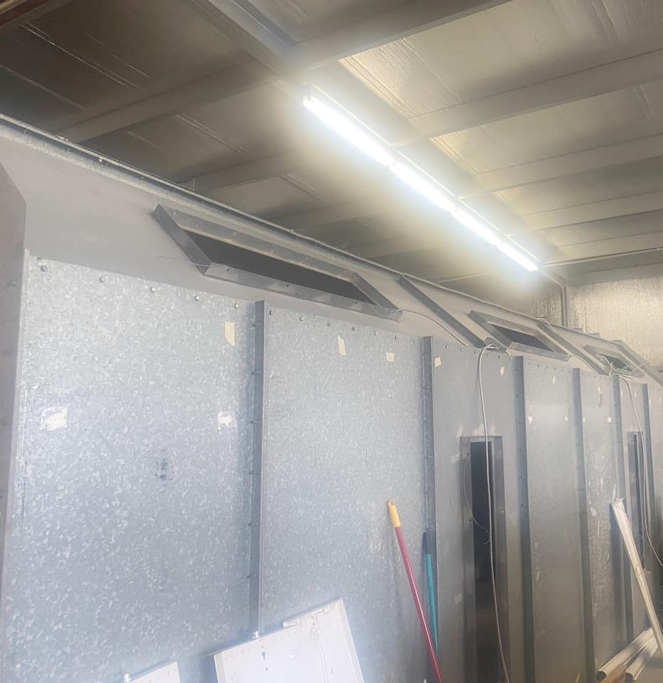 Low-angle view of a grey industrial workspace with long, sloped metal panels and rectangular vents under a bright light.