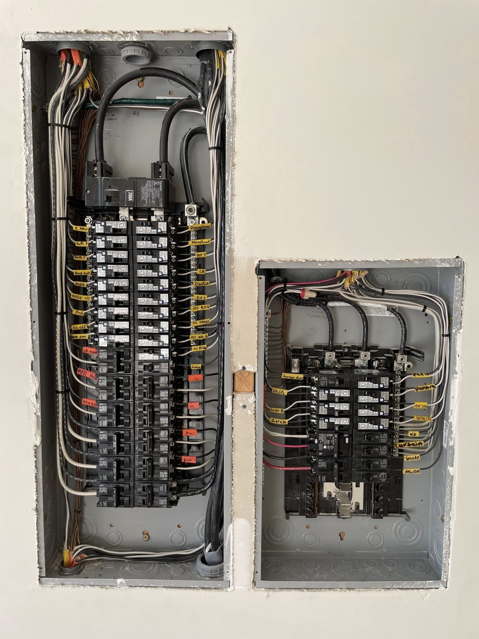 Two open electrical service panels side-by-side, revealing circuit breakers and various connected electrical wires.