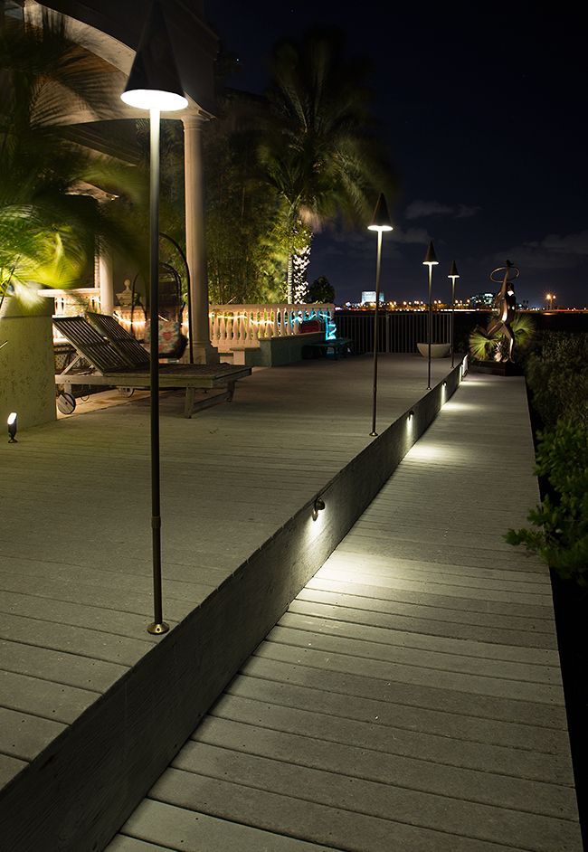 Illuminated wooden boardwalk at night with palm trees and modern lamp posts along the path