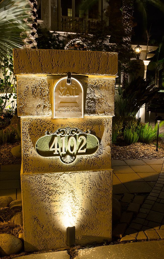 Illuminated stone pillar with house number 4102 in a garden at night