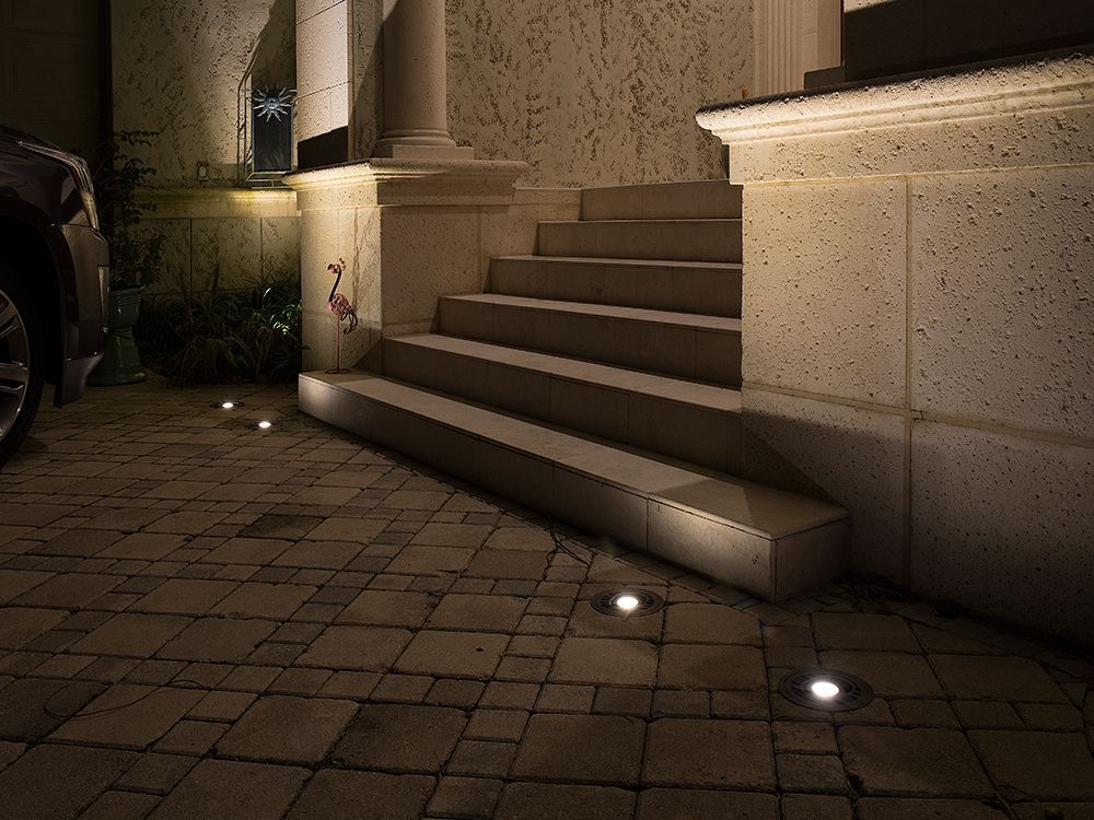 Nighttime front steps with small path lights beside a parked car and house exterior