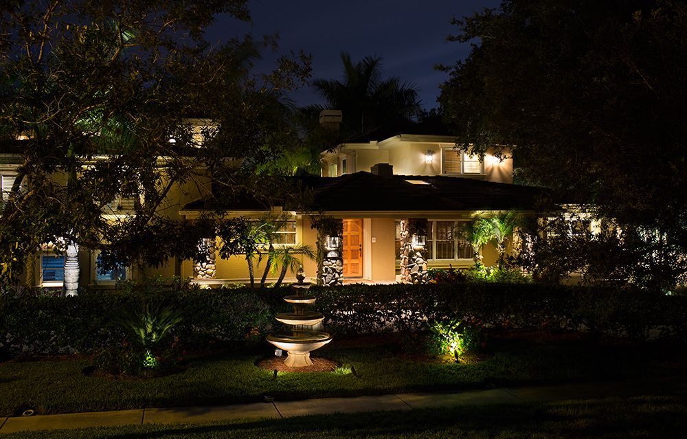 Night view of a lit house with garden lights and a central fountain in front