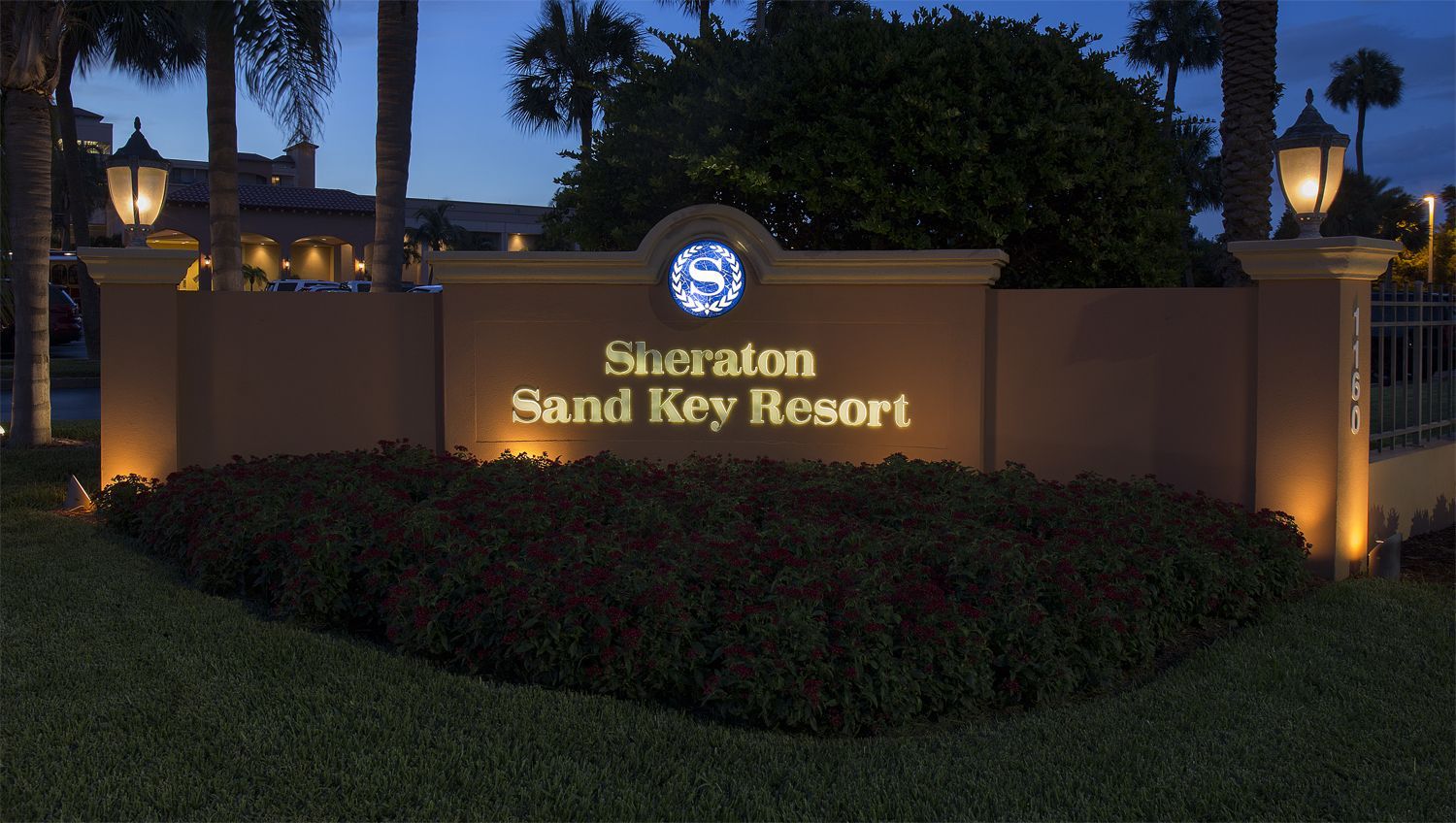 Lit resort sign reading “Sheraton Sand Key Resort” at dusk, with palm trees and landscape lighting