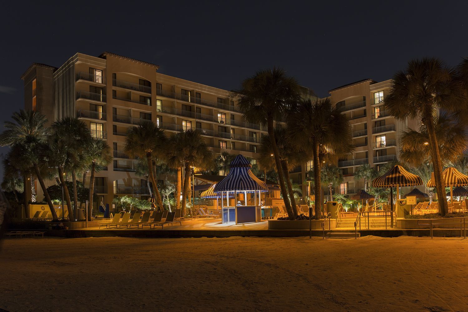 Nighttime view of a lit resort building with palm trees and a gazebo in the center