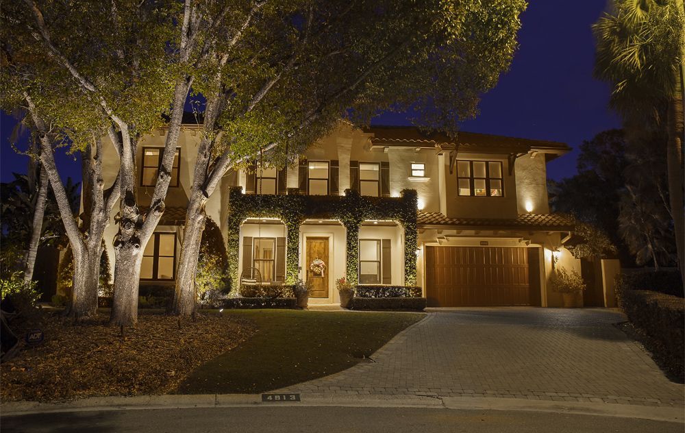 Illuminated two-story house at night with lit windows, large tree, and curved driveway