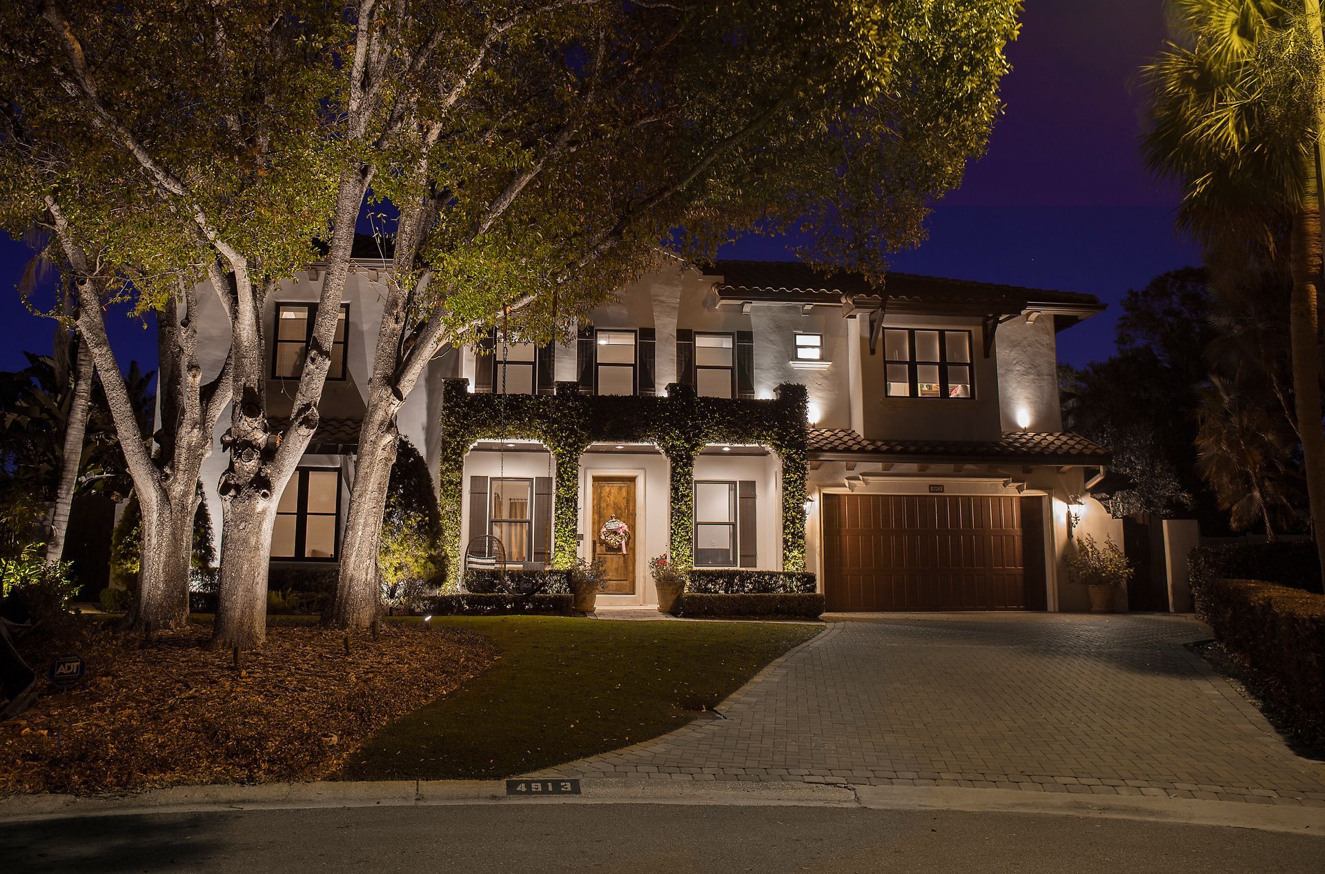 Two-story house at night with lit windows, a garage, and trees in the front yard