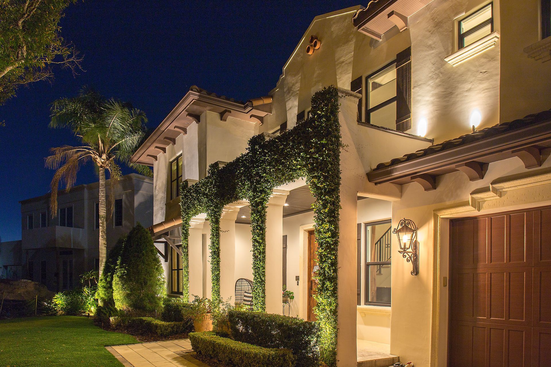 Lit stucco townhouse with ivy-covered columns along a walkway at dusk