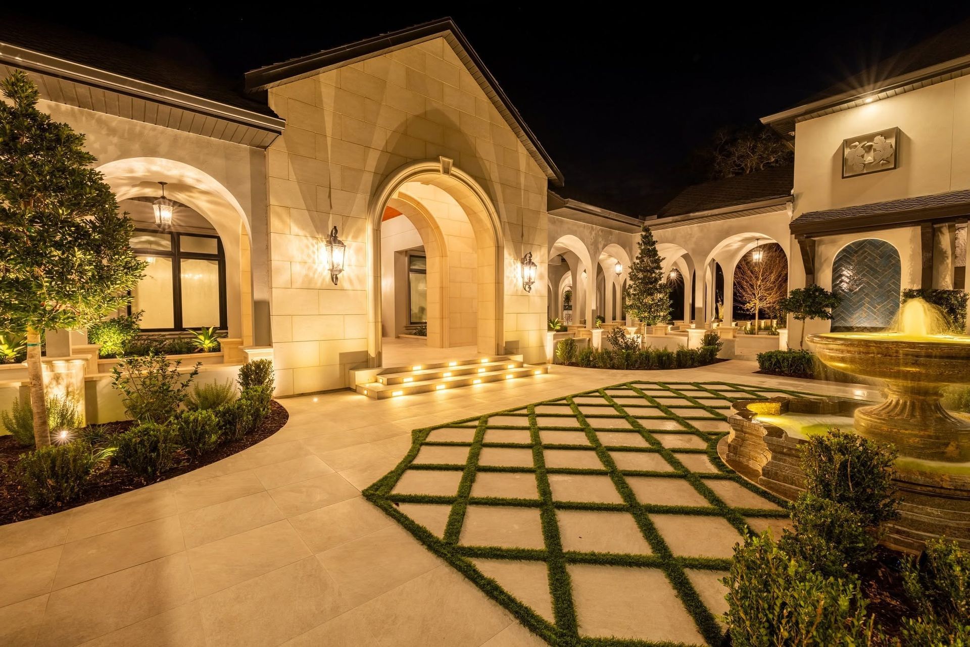 Elegant Mediterranean-style courtyard at night, warmly lit with arched windows and a geometric stone walkway.