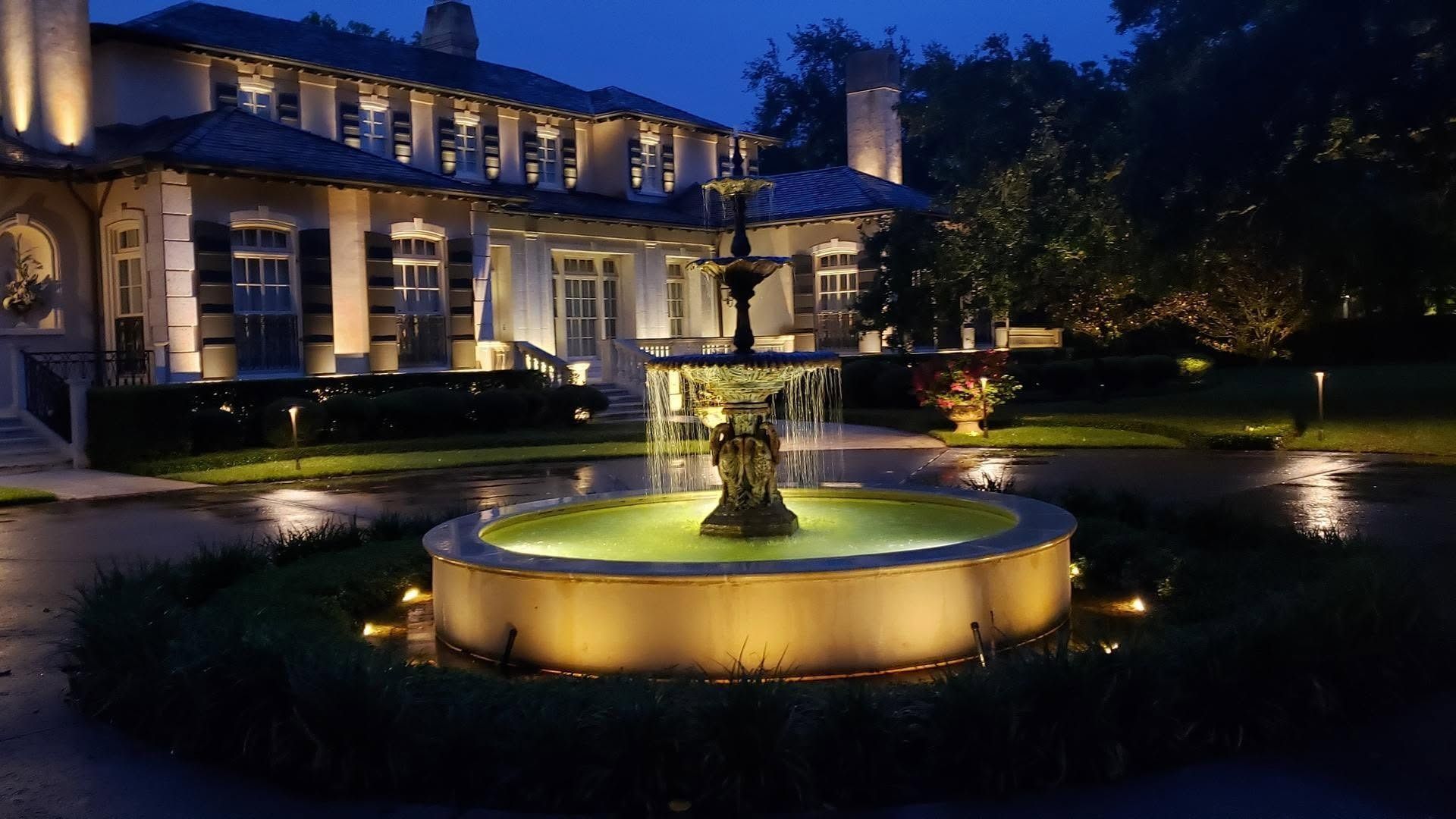 Illuminated mansion courtyard with a glowing circular fountain at night