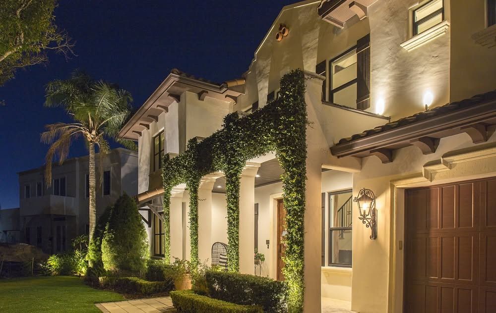Illuminated stucco townhouse exterior at night with palm trees and ivy-covered arches