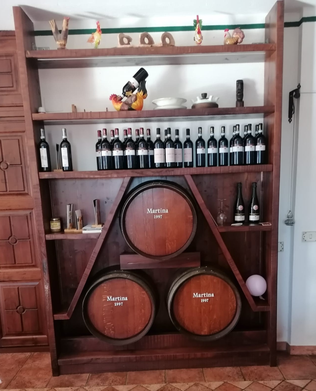 Una grande rastrelliera in legno che contiene numerose bottiglie di vino su ripiani e tre botti decorative.
