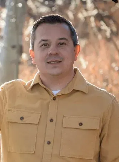 A man in a yellow shirt is standing in front of a tree.