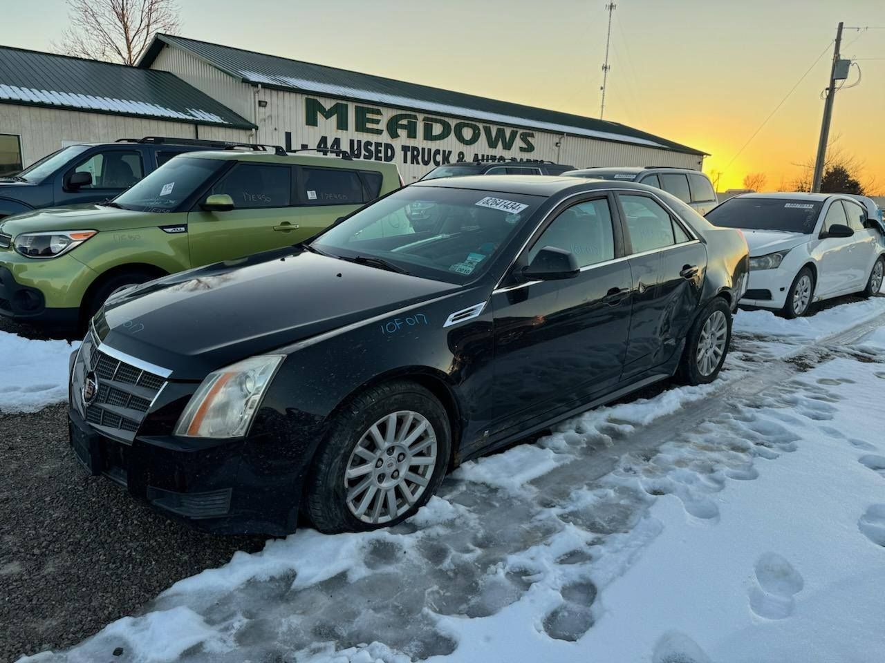 A black car is parked in the snow in front of a car dealership.