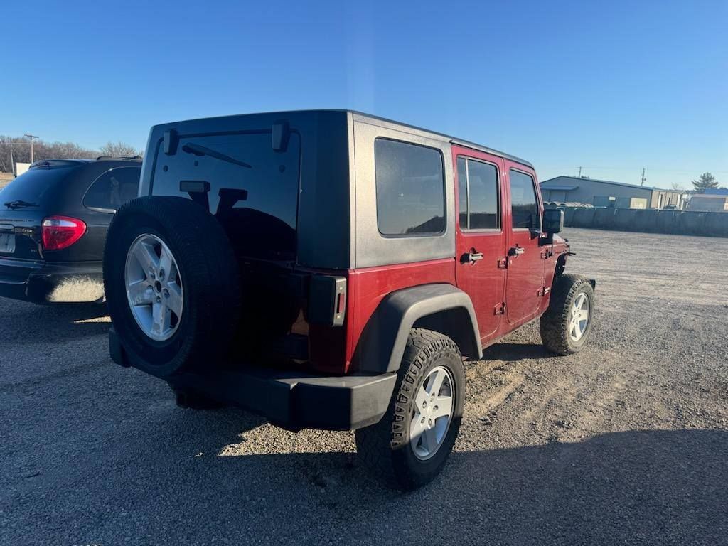 A red jeep is parked in a gravel lot.