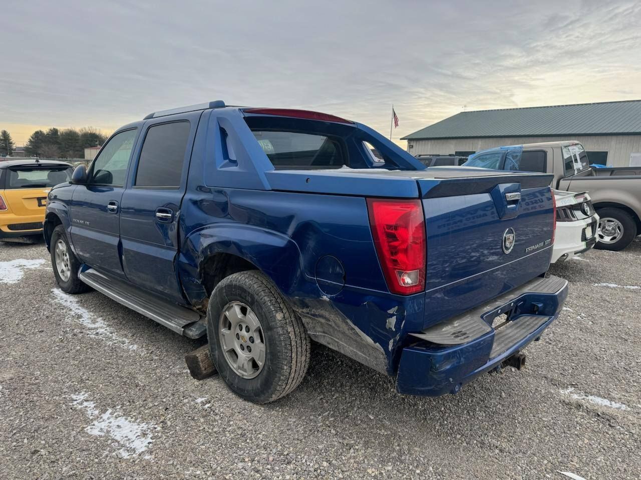 A blue pickup truck is parked in a gravel lot.