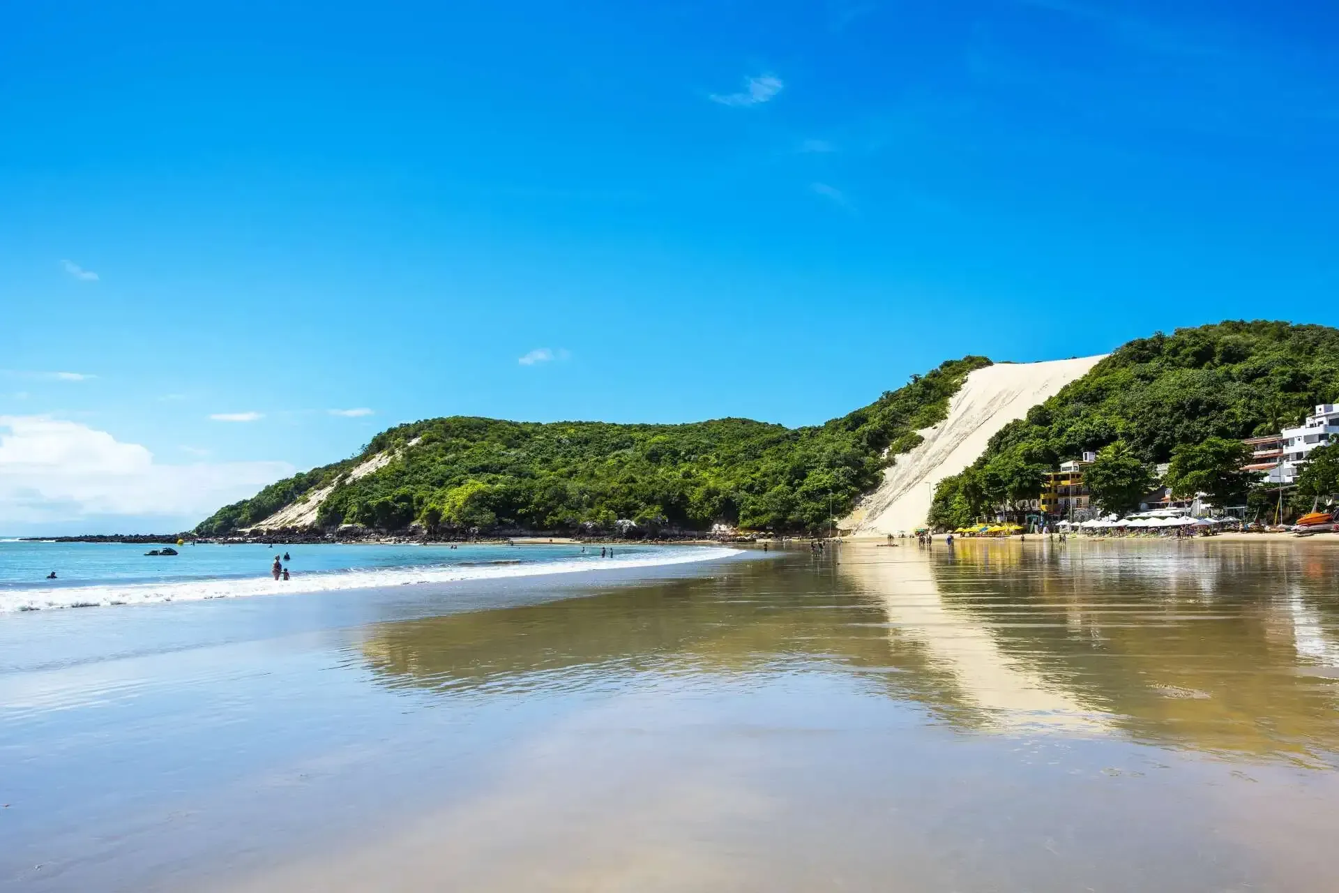 Uma praia com uma montanha ao fundo e um céu azul. - Pizzato Praia Hotel
