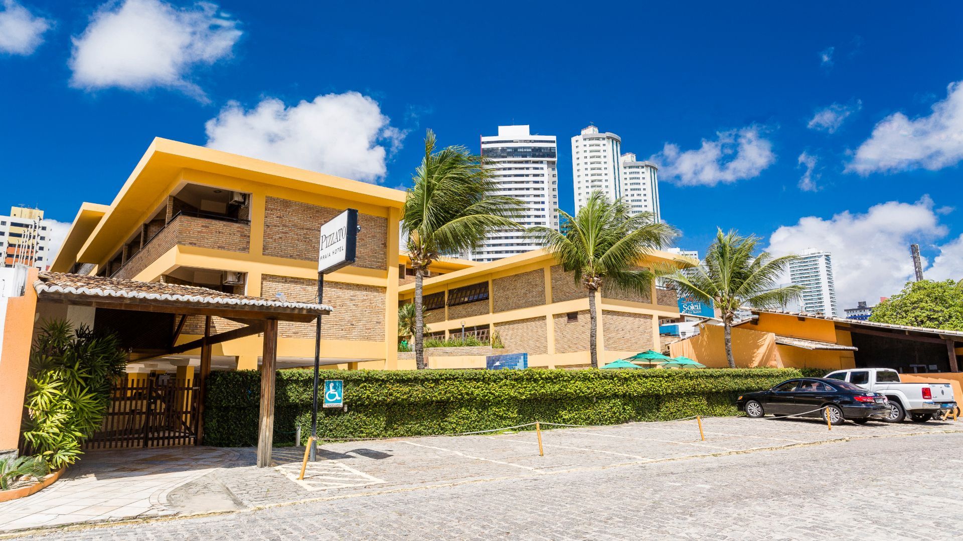 Um grande edifício com muitos carros estacionados na frente. - Pizzato Praia Hotel