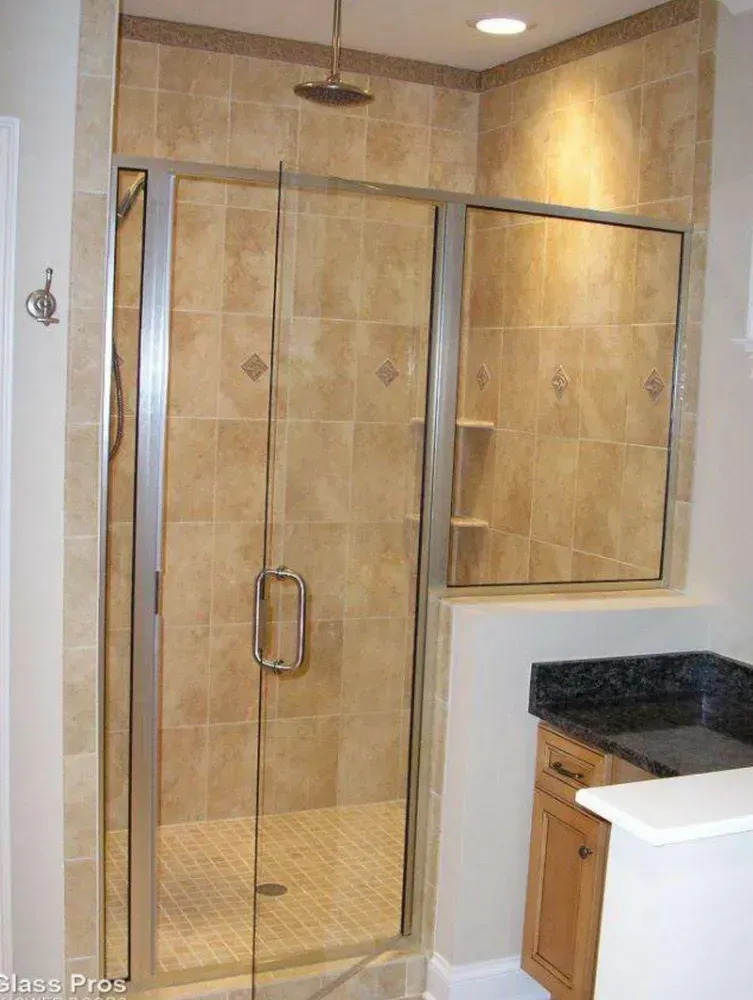 Glass-enclosed shower with beige tile walls and a marble countertop in a bathroom