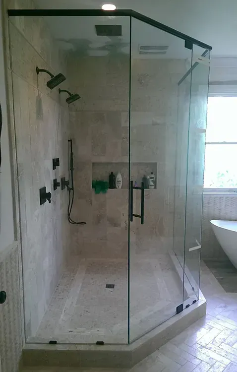 Glass corner shower stall in a bathroom with chrome fixtures and white tiled walls